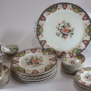 May include: A complete vintage porcelain dinnerware set featuring a floral design with orange, blue, and green accents. The set includes plates, bowls, cups, saucers, and a serving platter, all with gold trim.