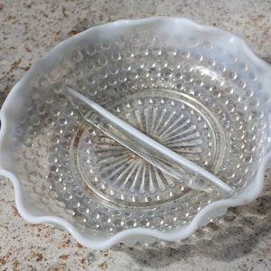 May include: A vintage, two-sectioned, white glass serving dish with a ruffled edge. The dish has a textured, hobnail pattern on the outer bowl and a clear, radial design in the center. A clear glass divider bisects the dish.