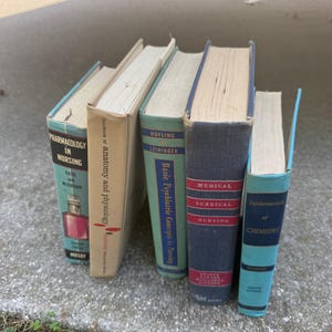 Puede incluir: Una colección de libros de texto de medicina y enfermería antiguos. Los libros tienen varios colores, incluyendo verde azulado, azul marino y beige. Los títulos incluyen "Farmacología en enfermería", "Enfermería médico-quirúrgica" y "Fundamentos de química".