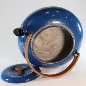 May include: A cobalt blue, spherical teapot with a matching lid. The teapot features a spout, a wooden handle, and a leather handle. The lid is off, revealing the interior. A vintage kitchenware item.