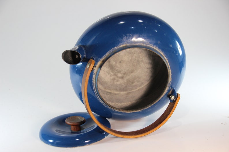 May include: A cobalt blue, spherical teapot with a matching lid. The teapot features a spout, a wooden handle, and a leather handle. The lid is off, revealing the interior. A vintage kitchenware item.