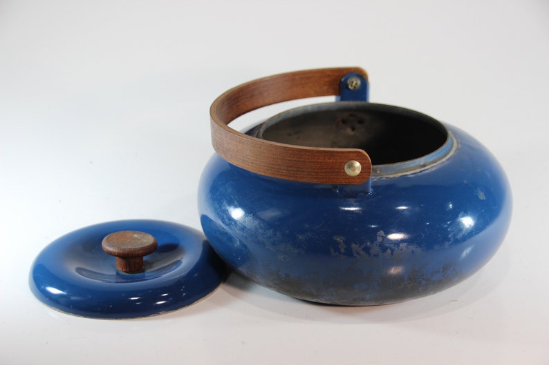 May include: A blue enamel kettle with a wooden handle and lid. The kettle has a round shape and a wooden handle that arches over the top. The lid has a wooden knob. The kettle is approximately 8 inches in diameter.