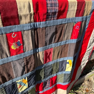 May include: A patchwork quilt with a variety of fabrics, including corduroy and patterned textiles. The quilt features a red border and blue accents, with a design that includes a horseshoe and a cowboy.