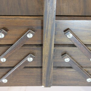 Puede incluir: Primer plano de una caja de costura de madera vintage. La caja es de color marr&oacute;n oscuro con tapa con bisagras y compartimentos extensibles. Los compartimentos se sujetan con tornillos met&aacute;licos.