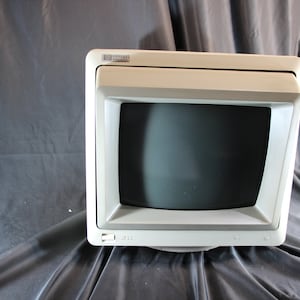 Puede incluir: Un monitor de ordenador vintage de color crema con una pantalla oscura. El monitor tiene forma cuadrada con una parte superior ligeramente inclinada y un pequeño panel de control en la parte inferior. El logotipo de HP es visible en la parte superior.