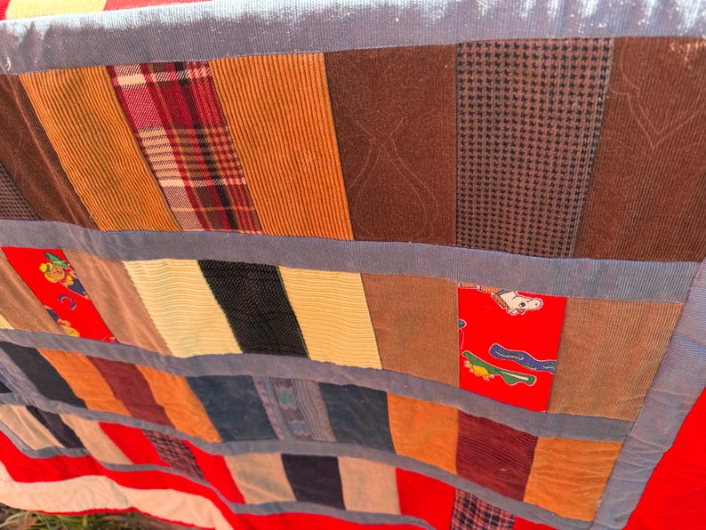 May include: A patchwork quilt with a variety of fabrics in shades of brown, orange, red, and blue. The quilt features corduroy, plaid, and patterned fabrics, with a red and white striped border.