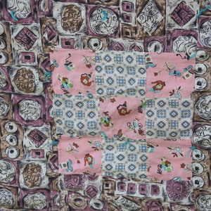 May include: A patchwork textile featuring a mix of patterns. The background has a repeating design of geometric shapes in brown, purple, and white. A pink square with floral and teapot motifs is sewn on top.