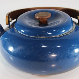 May include: A vintage blue enamel teapot with a wooden handle and lid knob. The teapot has a rounded body, a spout, and a lid. The wooden handle arches over the top, and the lid has a small wooden knob. The teapot is a classic kitchenware item.