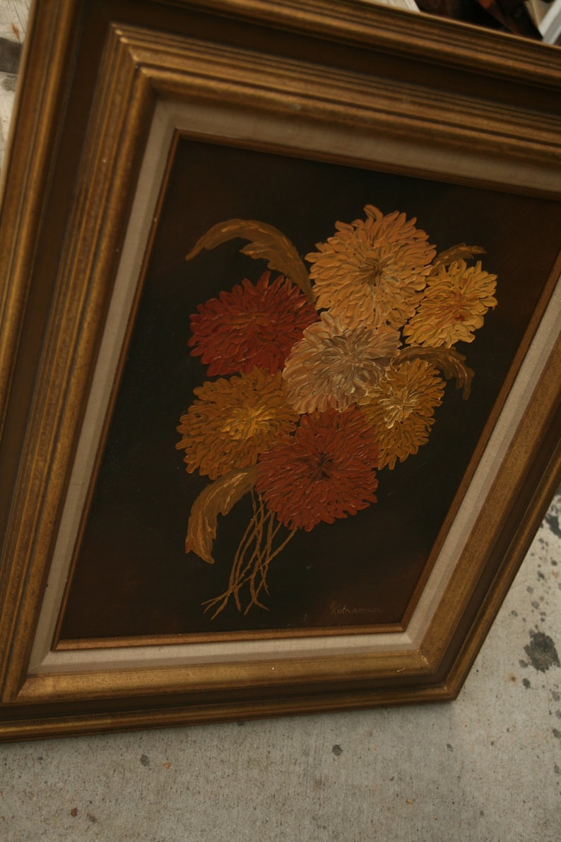 May include: A framed floral painting featuring a bouquet of orange, red, and yellow flowers against a dark brown background. The flowers are painted with textured brushstrokes, and the frame is gold-colored.