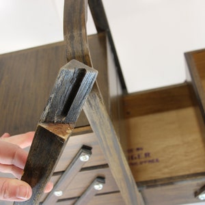 Puede incluir: Una caja de costura de madera vintage con un acabado marr&oacute;n oscuro. La caja tiene m&uacute;ltiples compartimentos y una tapa con bisagras. La caja es de madera y tiene un dise&ntilde;o cl&aacute;sico. La caja est&aacute; abierta, revelando el interior. La caja es de la marca Singer.