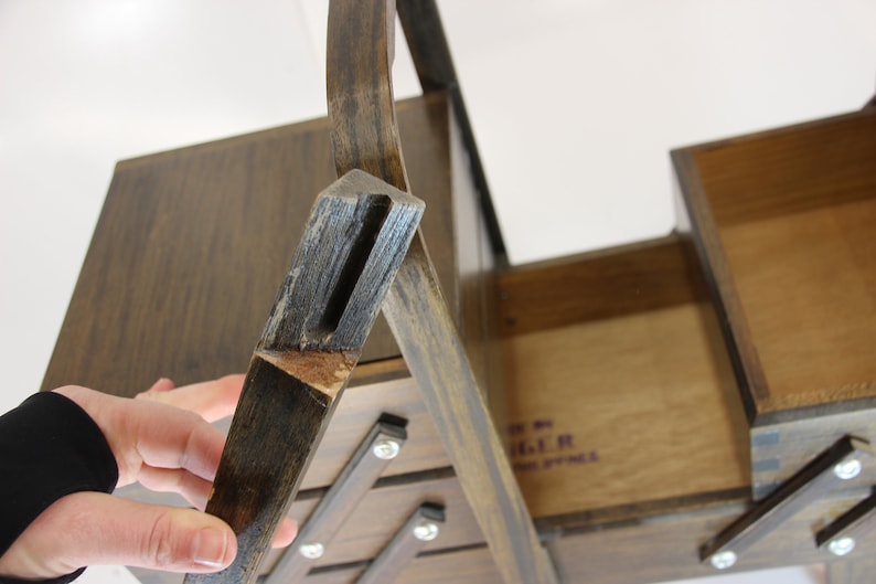Puede incluir: Una caja de costura de madera vintage con un acabado marr&oacute;n oscuro. La caja tiene m&uacute;ltiples compartimentos y una tapa con bisagras. La caja es de madera y tiene un dise&ntilde;o cl&aacute;sico. La caja est&aacute; abierta, revelando el interior. La caja es de la marca Singer.