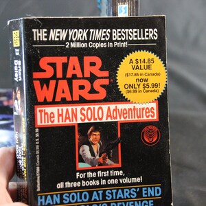 May include: A paperback book titled "Star Wars: The Han Solo Adventures" with a black cover and red lettering. The cover features an image of Han Solo holding a blaster. The book is a New York Times bestseller.