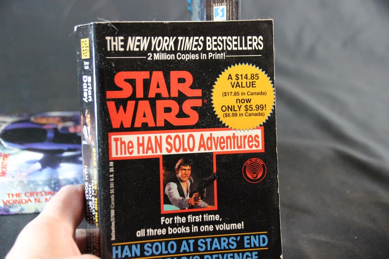 May include: A paperback book titled "Star Wars: The Han Solo Adventures" with a black cover and red lettering. The cover features an image of Han Solo holding a blaster. The book is a New York Times bestseller.