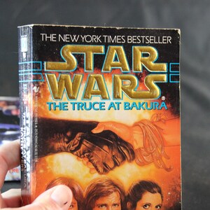 May include: A hardcover book titled "Star Wars: The Truce at Bakura" with gold lettering and a vibrant cover illustration. The book is a New York Times bestseller. The cover art depicts a handshake and character portraits.