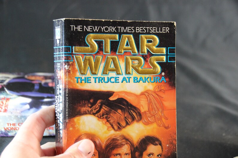 May include: A hardcover book titled "Star Wars: The Truce at Bakura" with gold lettering and a vibrant cover illustration. The book is a New York Times bestseller. The cover art depicts a handshake and character portraits.