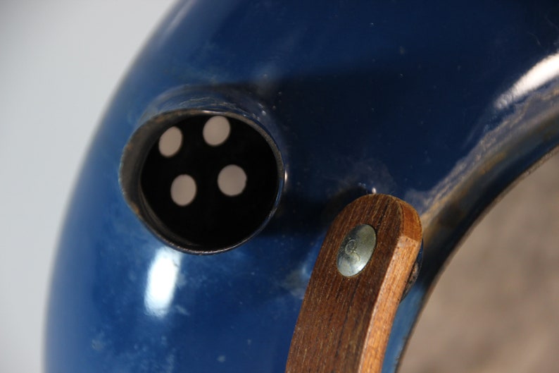 May include: Close-up of a blue object with a circular opening featuring four white dots. A wooden handle is attached with a metal fastener. The object has a glossy finish and a curved shape.