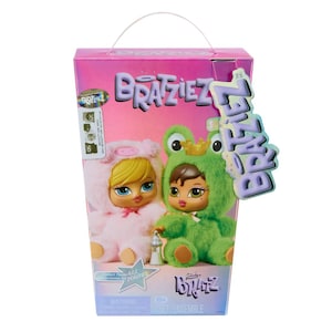Puede incluir: Una caja rosa con asa presenta dos muñecas Bratz. Una muñeca viste un disfraz de conejito rosa, la otra un disfraz de rana verde. La caja tiene la palabra "Bratziez" en un degradado rosa y morado.
