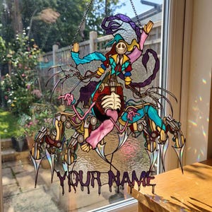 Könnte beinhalten: Buntes Glasfenster-Dekoration mit einer skurrilen Kreatur mit skelettartigem Torso, mechanischen Gliedmaßen und einem lächelnden Gesicht. Der Text "YOUR NAME" befindet sich unten. Das Design enthält Farbtöne von Blau, Lila, Rosa und Gelb.