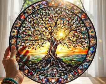 May include: A round stained glass panel depicting a tree with a vibrant sunset background. The tree has a detailed trunk and branches with colorful leaves. The panel is held by a hand and has a black metal frame.