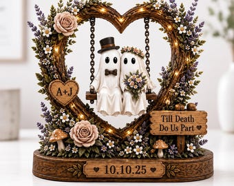 May include: A decorative tabletop ornament featuring two ghost figures in wedding attire sitting on a swing inside a heart-shaped frame. The frame is adorned with flowers, mushrooms, and lights. It includes the text A+J, Till Death Do Us Part, and 10.10.25.