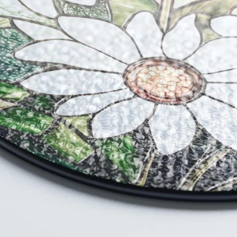 Puede incluir: Decoraci&oacute;n redonda de vidriera con dise&ntilde;o de margarita. La flor tiene p&eacute;talos blancos y centro marr&oacute;n, con hojas verdes y borde negro. El vidrio tiene un acabado texturizado. Adecuado para la decoraci&oacute;n del hogar.