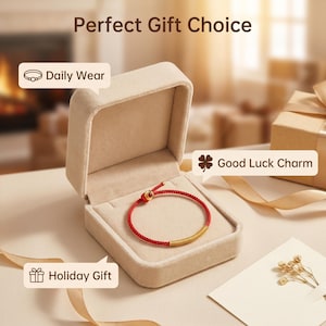 May include: A red cord bracelet with a gold-toned cylindrical accent and a small red bead, presented in an open beige velvet jewelry box. The image includes text reading Perfect Gift Choice, Daily Wear, Good Luck Charm, and Holiday Gift.