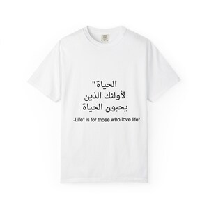 Può includere: T-shirt bianco con testo nero in arabo e inglese. Il testo arabo si traduce in "La vita è per coloro che amano la vita". La maglietta ha un girocollo e maniche corte. La maglietta è realizzata in un materiale morbido e confortevole.