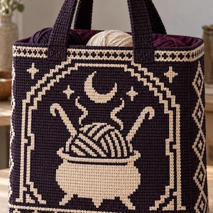 May include: A dark purple crochet tote bag featuring a cream-colored geometric border and a central graphic of a cauldron filled with yarn, with two knitting needles and a crescent moon above it. The bag has two sturdy handles and a deep interior.