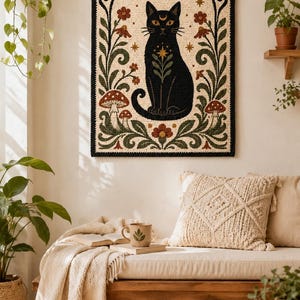 May include: A rectangular wall hanging featuring a black cat centered within an arched frame. The design includes a golden crescent moon, stars, red flowers, green foliage, and mushrooms, all rendered in a textured, punch needle style.