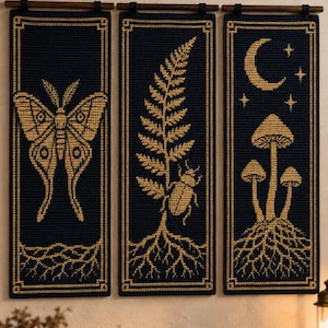 May include: Three rectangular dark navy blue crochet wall hangings with gold-colored yarn details. The left panel features a moth, the center panel shows a fern and a beetle, and the right panel depicts three mushrooms under a crescent moon and stars.