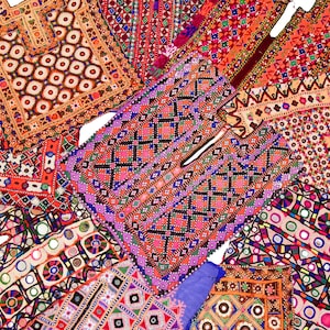 May include: A selection of brightly coloured, embroidered textiles. The pieces display intricate geometric patterns in shades of red, orange, purple, and blue. The textiles appear handmade, with detailed stitching and embellishments.