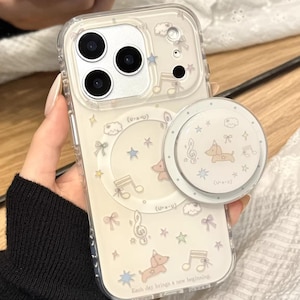 Könnte beinhalten: Transparente Handyhülle mit cremefarbenem Hintergrund, verziert mit Noten, Sternen, Schleifen und einem Cartoon-Hund. Die Hülle hat einen passenden Pop-Socket. Der Text "Kash day brings a new beginning" ist sichtbar. Der Text "Cute V Case" ist ebenfalls sichtbar.