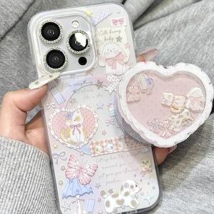 Pode incluir: Capa de telefone transparente com um design decorativo com um coelho, um cão e uma borboleta. A capa tem um pop socket em forma de coração com pequenos elementos decorativos no interior. O texto "Cute V Case" é visível.