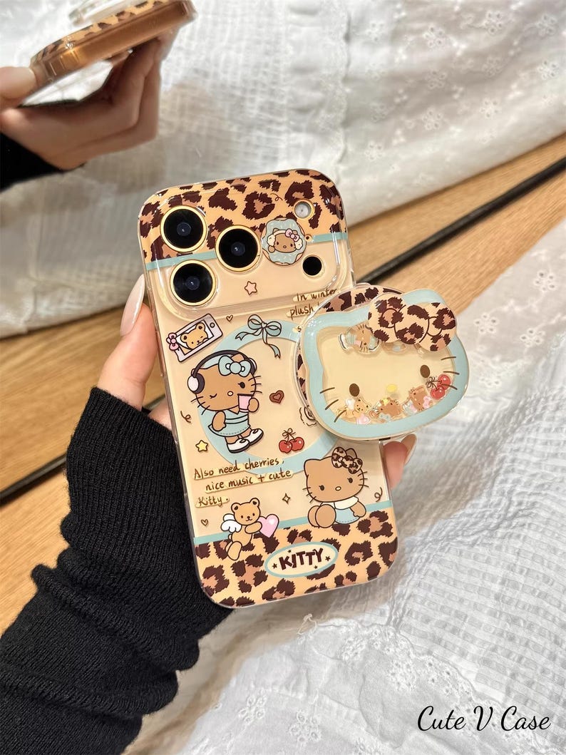 May include: A clear phone case with a leopard print design and cartoon illustrations of a cat. The case has a matching pop socket. Text on the case includes "Kitty" and "Cute V Case".