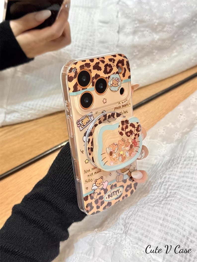 May include: A clear phone case with a leopard print design and a pop-up grip featuring a cartoon bear and other characters. The case has the word "KITTY" and the text "Also need nice music Kitty".