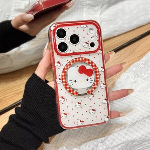May include: Clear phone case with a red border and a white background covered in small red Hello Kitty faces. The case has a red and white gingham ring holder with a Hello Kitty face and a red bow. The text "Cute V Case" is at the bottom.
