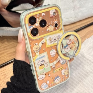 May include: A clear phone case with a light orange background and cartoon character stickers. The case has a built-in ring holder with cartoon characters. The text "Cute V Case" is at the bottom.
