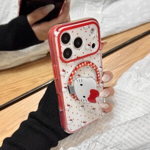 May include: A red and white phone case with a Hello Kitty design. The case has a clear back with a pattern of small red hearts and Hello Kitty faces. The edges are red, and the case has a ring holder with a Hello Kitty face. The text "Cute V Case" is at the bottom.