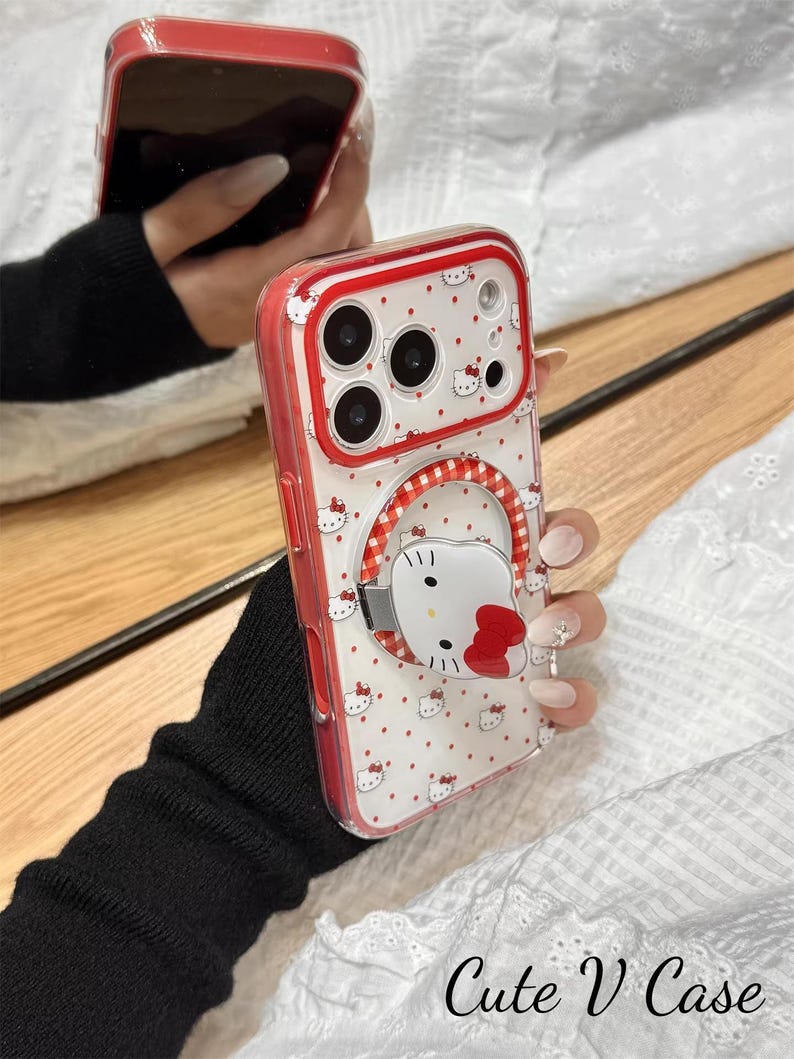 May include: A red and white phone case with a Hello Kitty design. The case has a clear back with a pattern of small red hearts and Hello Kitty faces. The edges are red, and the case has a ring holder with a Hello Kitty face. The text "Cute V Case" is at the bottom.