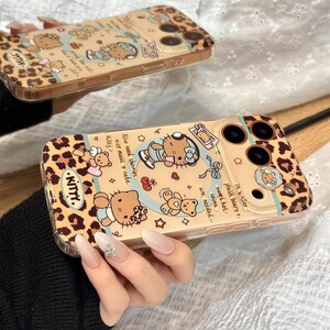 May include: Two phone cases with a leopard print design and cartoon illustrations of a cat, teddy bears, and text. The cases are tan with black and brown accents. One case has the word "KITTY" in a pink font.