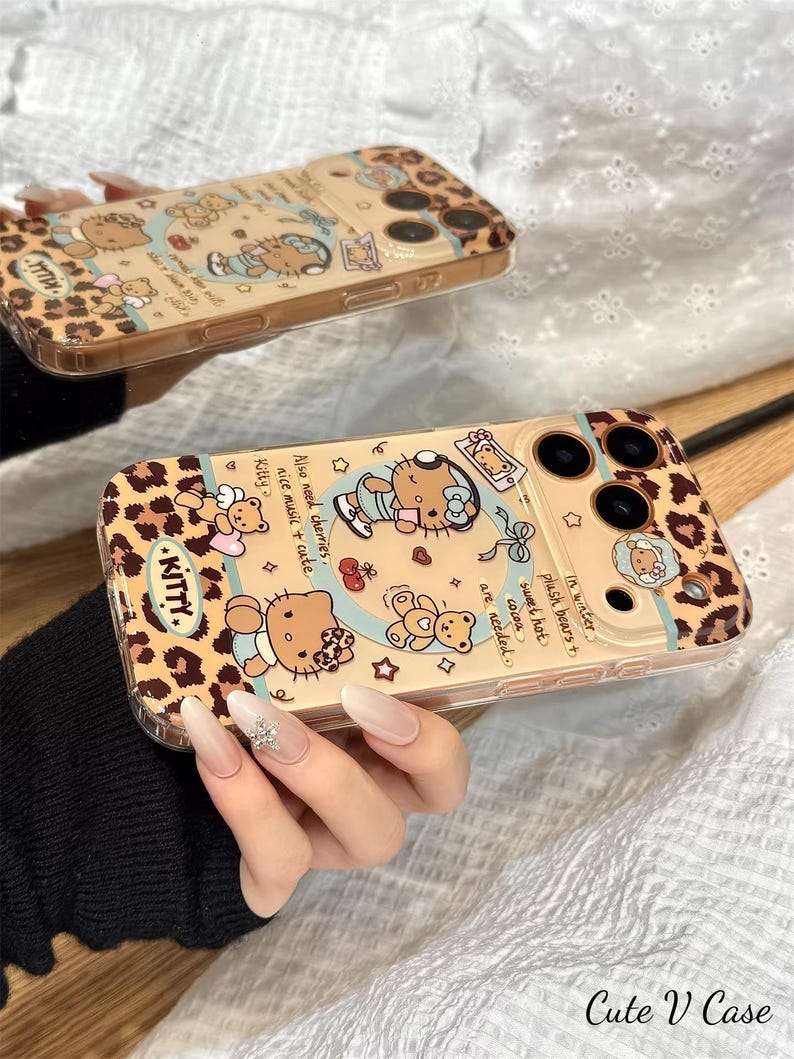 May include: Two phone cases with a leopard print design and cartoon illustrations of a cat, teddy bears, and text. The cases are tan with black and brown accents. One case has the word "KITTY" in a pink font.