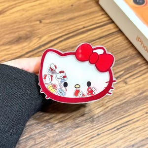 May include: A clear phone case with a red-outlined Hello Kitty design and a red bow. The case has a white interior with small Hello Kitty figures. The text "Cute V Case" is at the bottom.