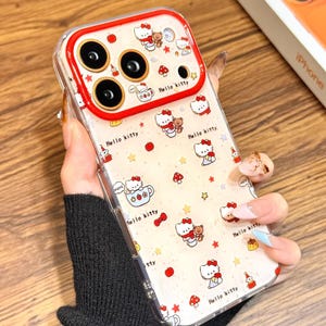 May include: Clear phone case with a Hello Kitty design and red detailing. The case features a red camera border and is decorated with Hello Kitty characters, stars, mushrooms, and the words "Hello Kitty". The text "Cute V Case" is also visible.