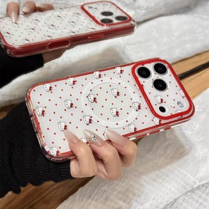 May include: Clear phone case with a red border, featuring a pattern of white Hello Kitty faces and red polka dots. The case has a circular design on the back and the text "Cute V Case".