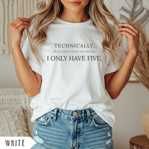 Op de afbeelding: Wit T-shirt met de tekst "TECHNICALLY, (if you don't count the chicks), I ONLY HAVE FIVE." Het shirt wordt gecombineerd met een blauwe spijkerbroek. Het woord "WHITE" staat onderaan de afbeelding.