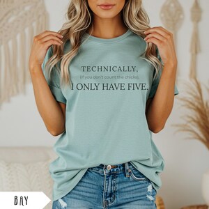 Op de afbeelding: Een witte keramische mok met een zwart handvat en de tekst "But First, Coffee" in een zwarte, handgeschreven lettertype. De mok staat op een wit oppervlak.