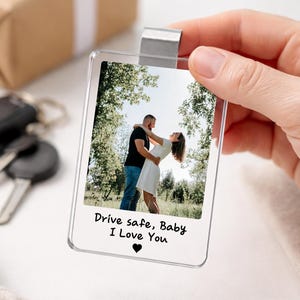 May include: A clear acrylic photo keychain with a metal clip. The photo shows a couple embracing outdoors. The text "Drive safe, Baby I Love You" is printed below the photo, with a heart symbol.