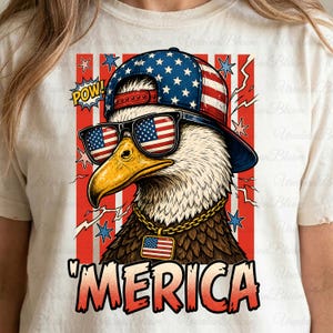 May include: A white t-shirt featuring a graphic of an eagle wearing sunglasses, a cap, and a gold chain, all adorned with the American flag design. The word "MERICA" is printed in red and white. The design includes stars, lightning bolts, and the word "POW!"