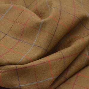 Puede incluir: Primer plano de una tela marrón con un patrón de cuadros. El estampado de cuadros presenta líneas que se cruzan en rojo, azul y morado. La tela está doblada, mostrando textura y profundidad. Ideal para ropa o decoración.