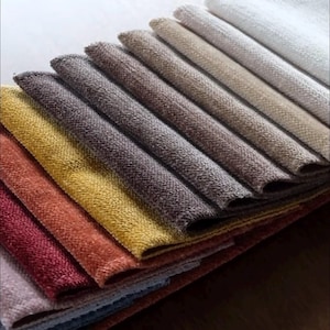 Puede incluir: Una colección de muestras de tela dispuestas en una pila superpuesta. Los textiles presentan una superficie tejida con textura y se muestran en un espectro de colores que incluye blanco, beige, marrón, gris, amarillo, naranja, rojo y rosa.